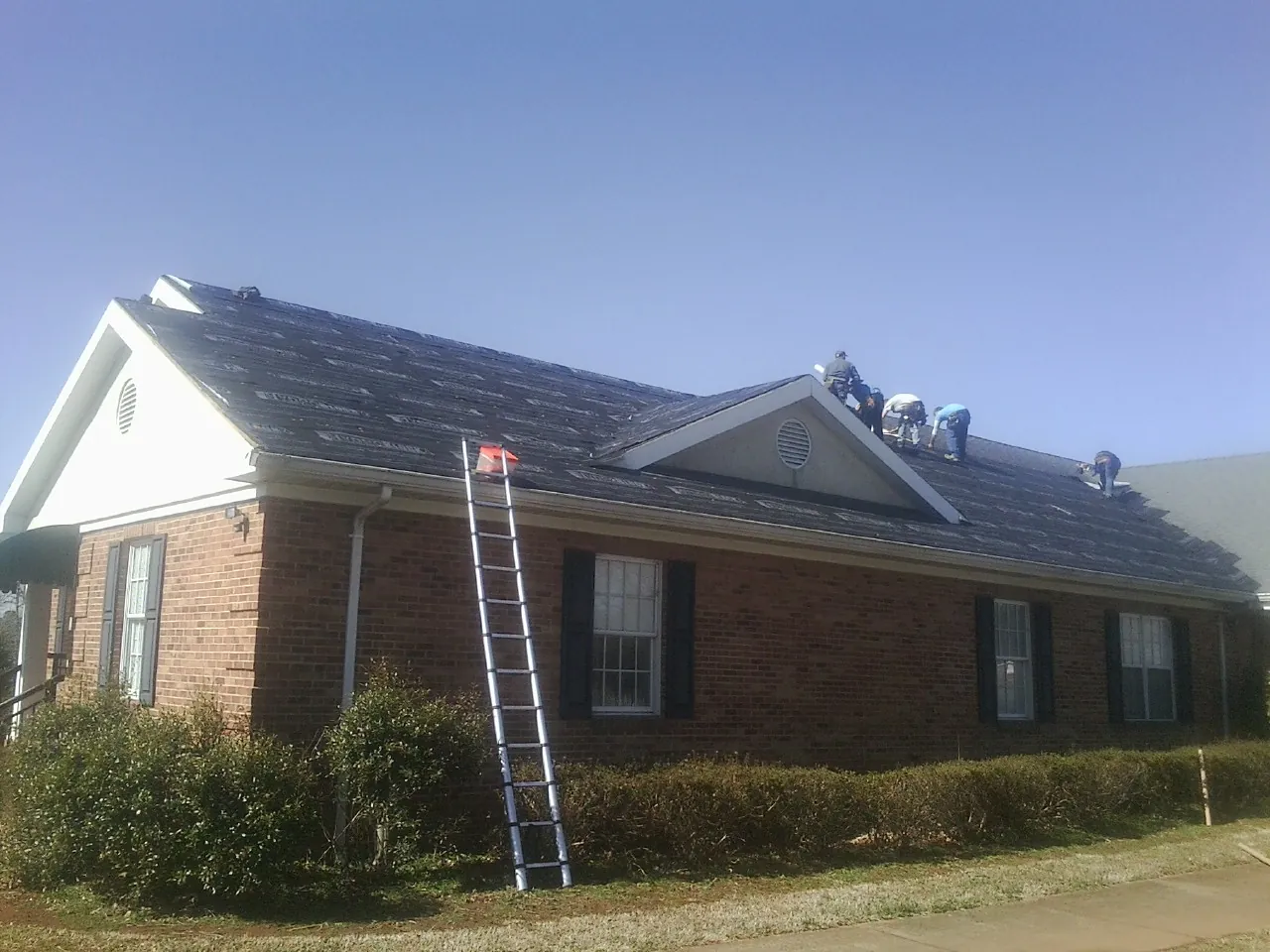 Crew tearing shingles off a brick ranch roof with a ladder set — Metal Roof Repair work by our crew in Otis Orchards