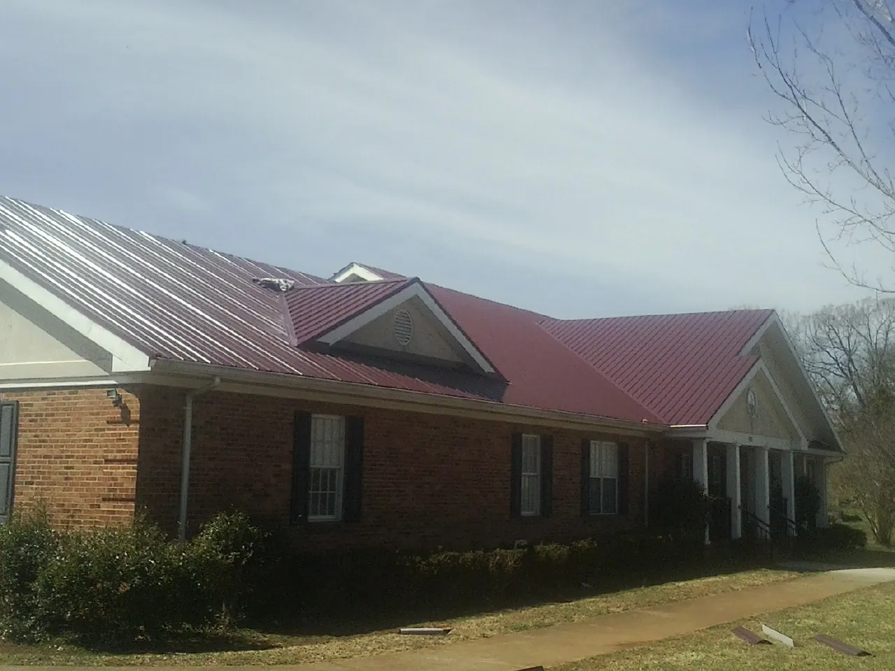 Red metal roof with gabled entries on a long brick building, from a Hail Damage Roof Repair job in Otis Orchards
