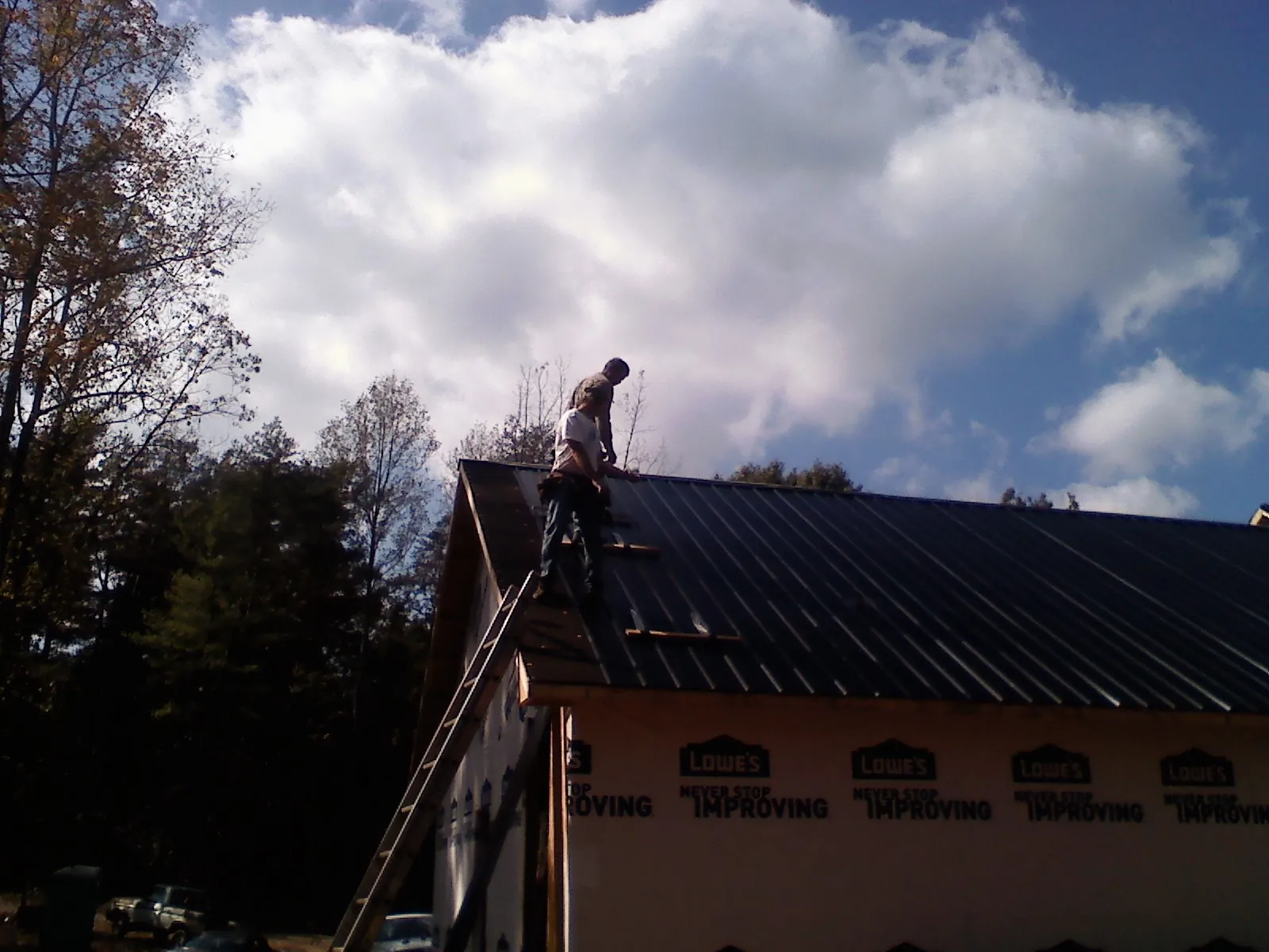 Roofer fastening dark metal panels high against a cloudy sky, from a Roof Inspection job in Otis Orchards