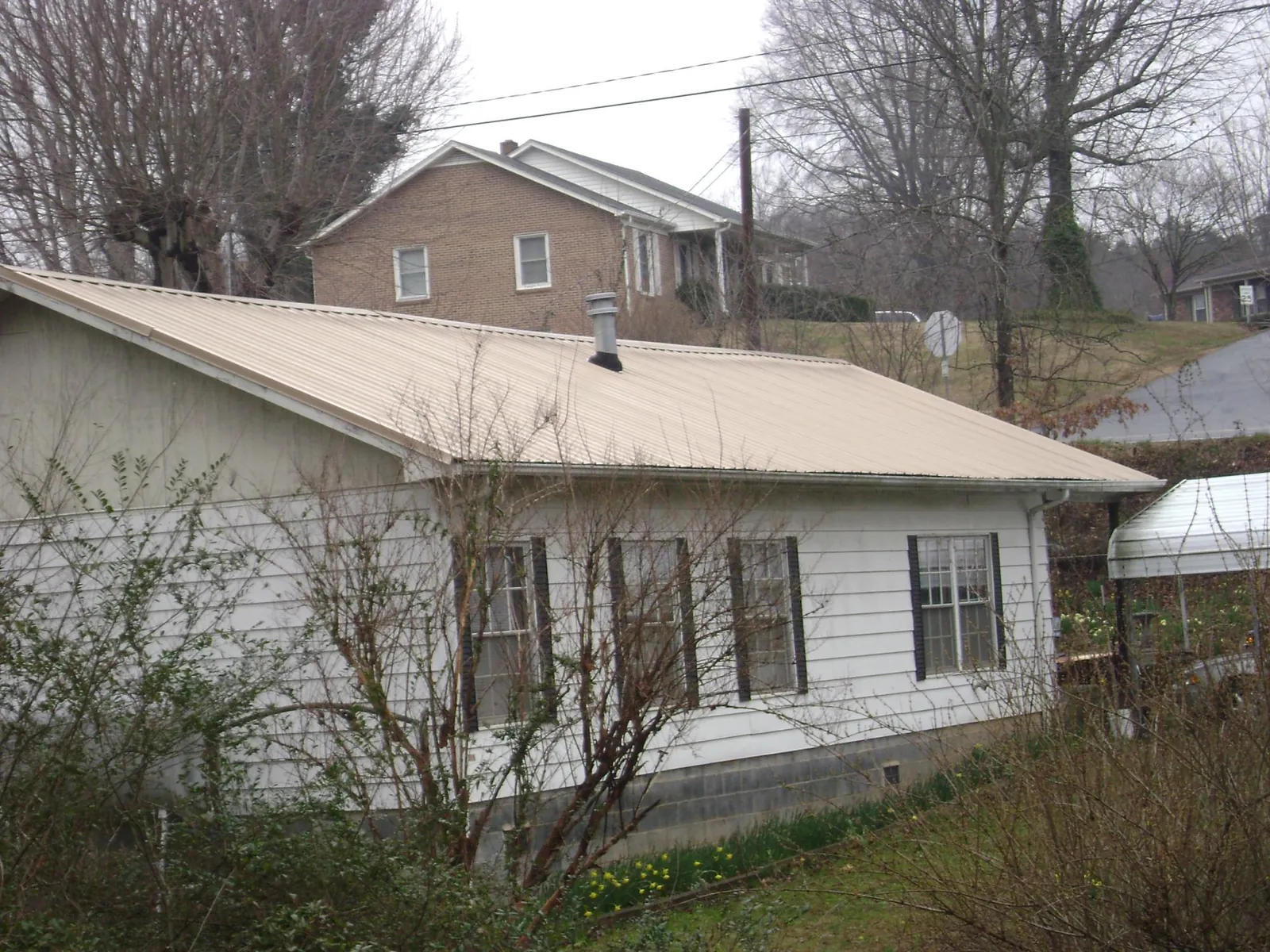 Tan metal roof on a white sided house set into a hillside — Commercial Roofing by Roofing Brothers in Otis Orchards
